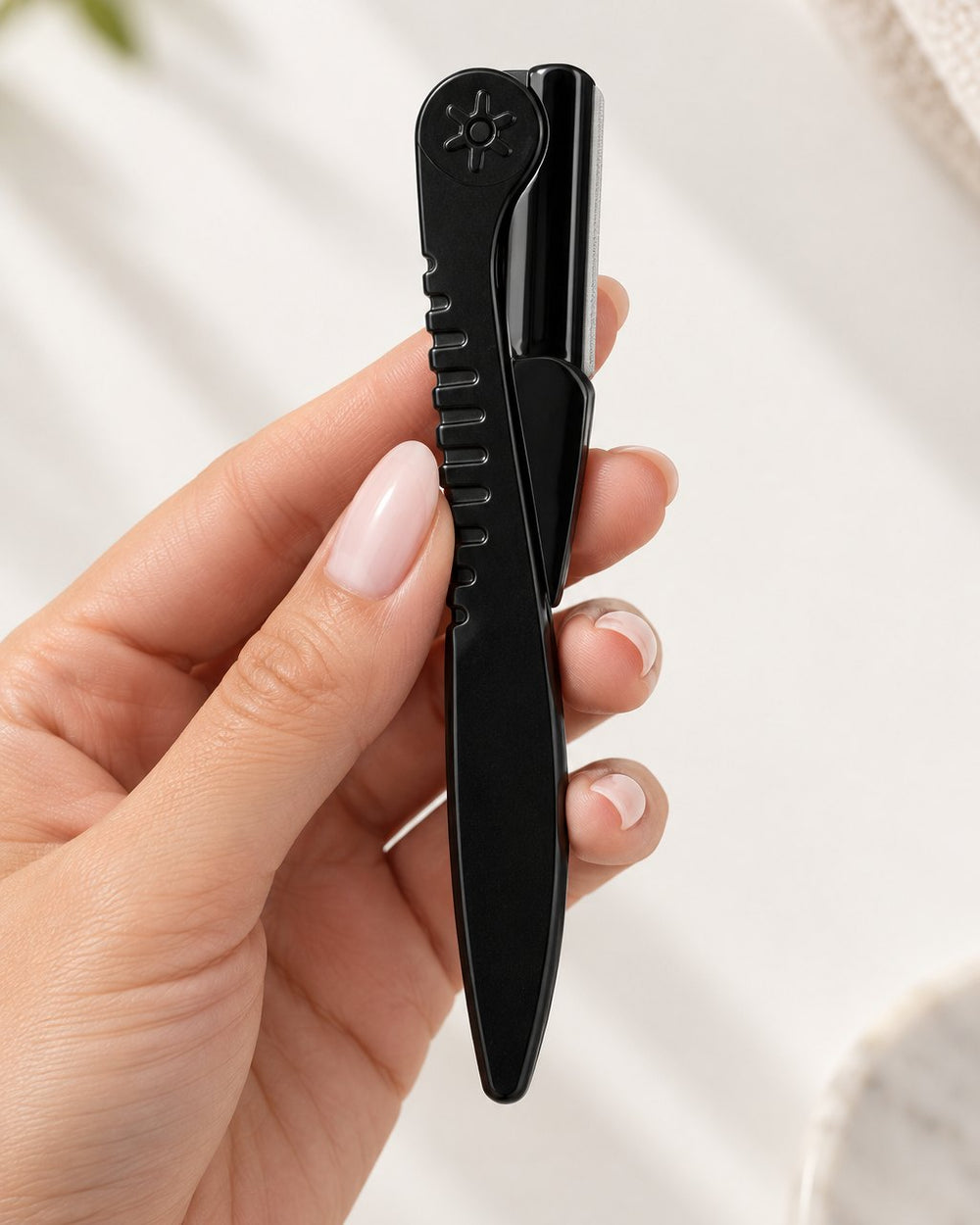 The razor folded flat between two fingers, about the length of a pen