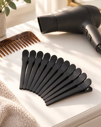 Black clips lined up on a dresser beside a comb and a hair dryer