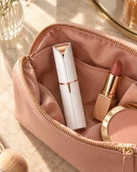 Facial hair remover in an open makeup bag beside a lipstick and a compact