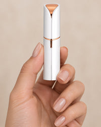 The facial hair remover held between thumb and fingers, the size of a lipstick