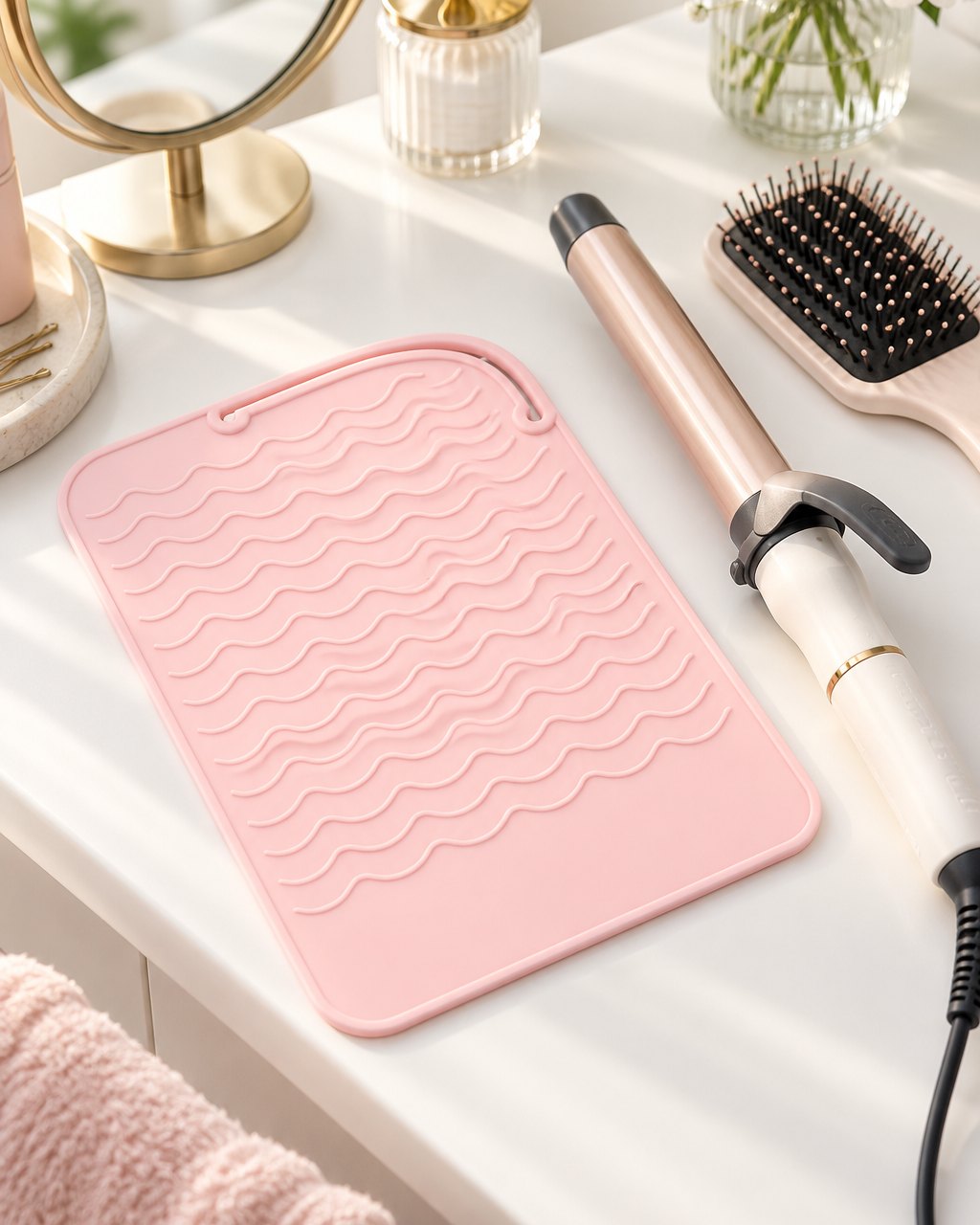 Pink heat mat on a vanity beside a curling wand and a hairbrush
