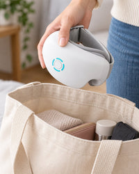 The eye massager folded in half and held in one hand above a tote bag