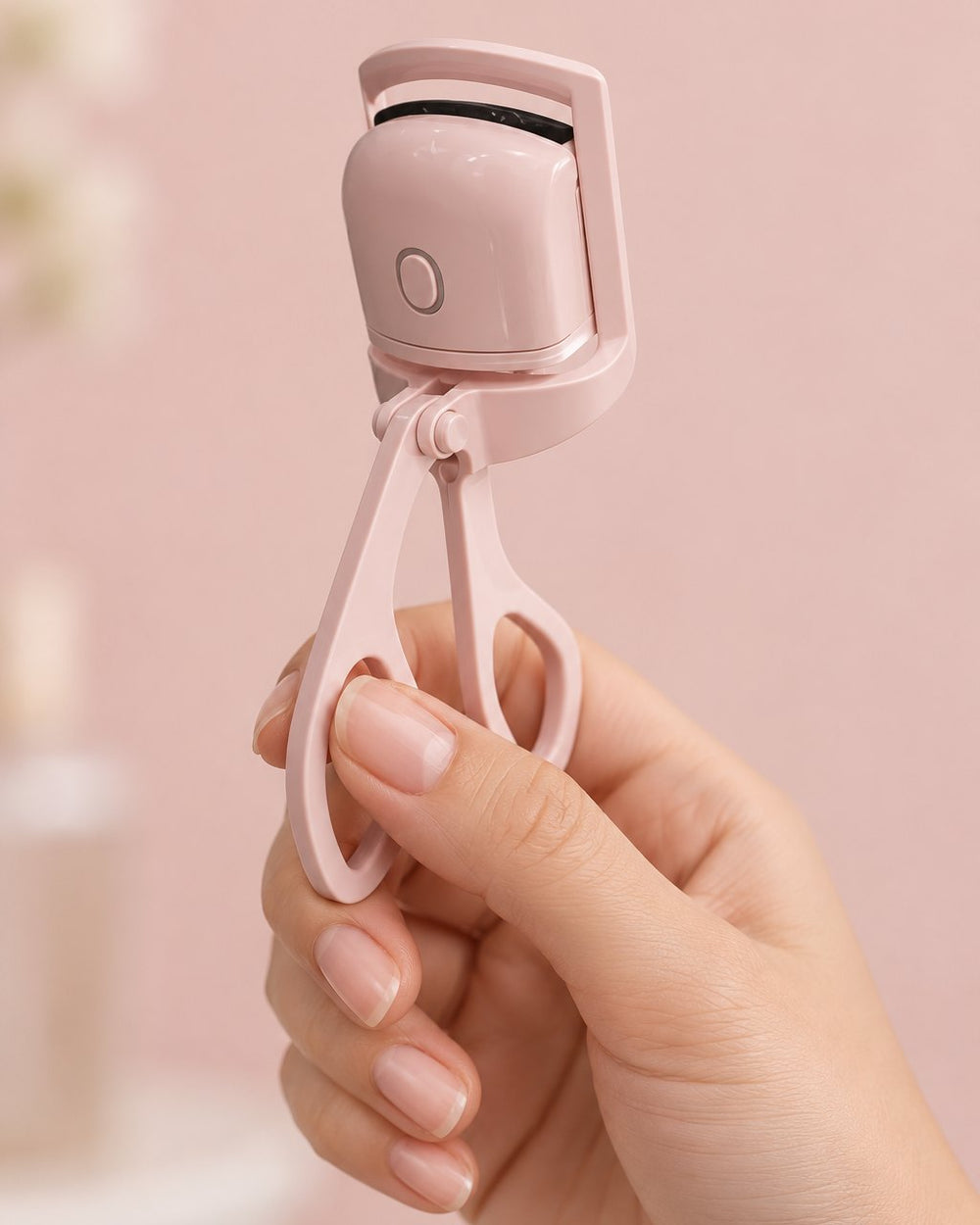 The heated curler held by its handles in one hand, the size of a regular lash curler