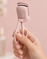 The heated curler held by its handles in one hand, the size of a regular lash curler