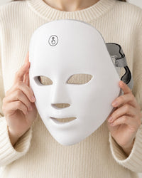 LED face mask held up in two hands, showing it covers a whole adult face