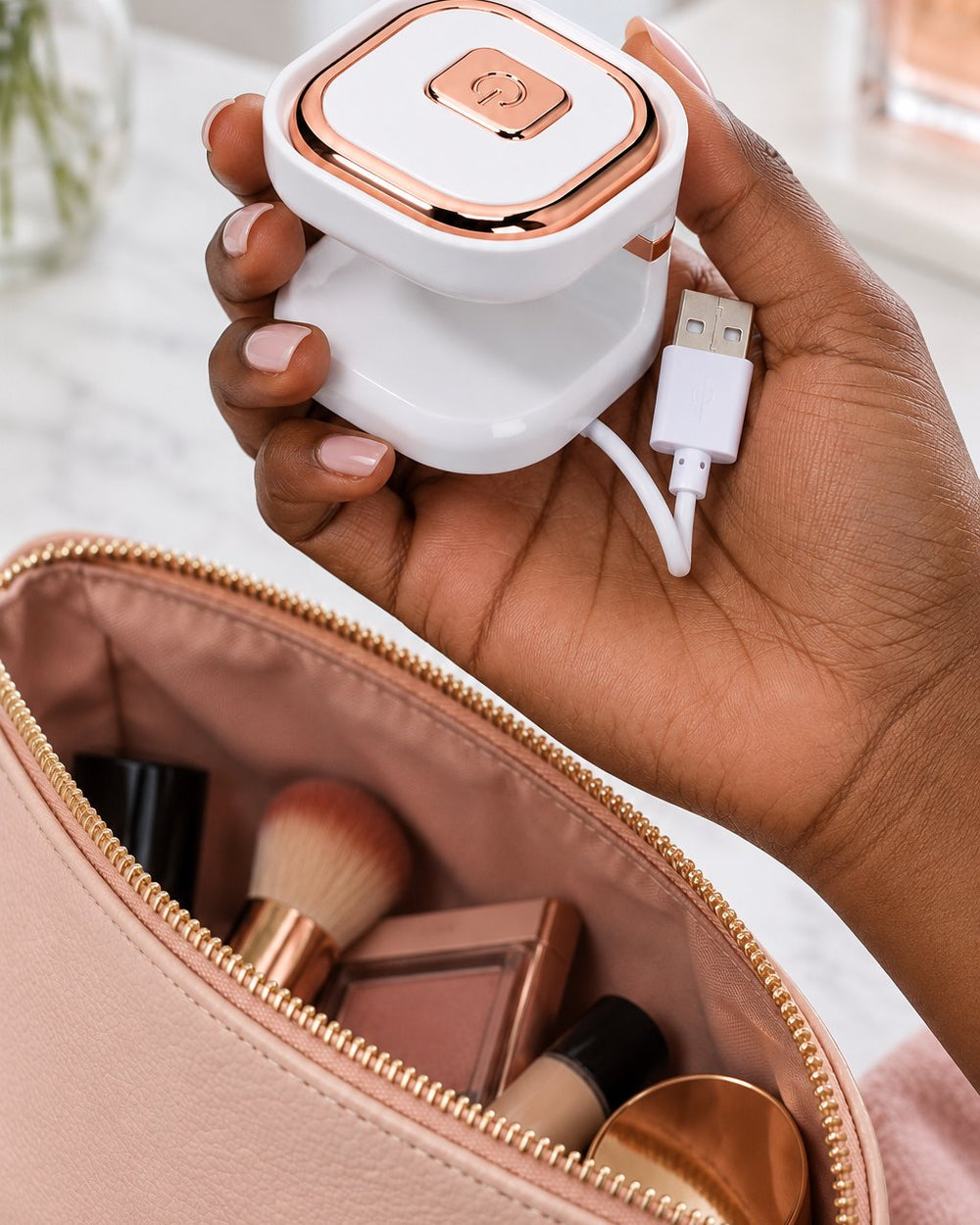 The mini nail lamp held in one hand above an open makeup bag