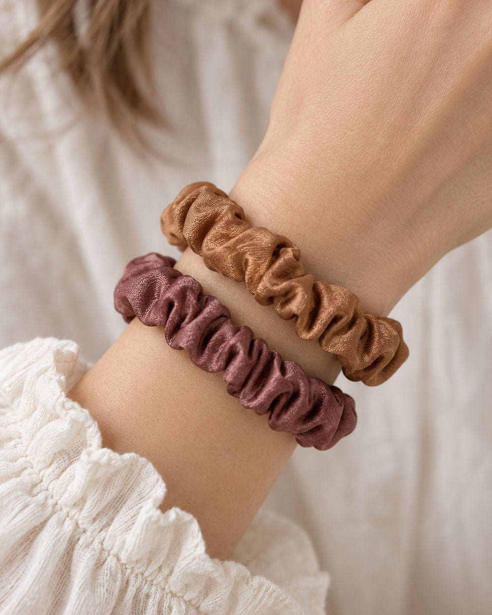 Two satin scrunchies worn on a wrist like bracelets