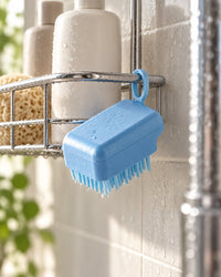 Blue scalp brush hanging by its loop from a shower caddy