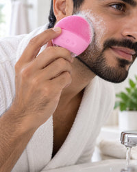 Man cleansing his cheek with the pink silicone brush over a bathroom sink