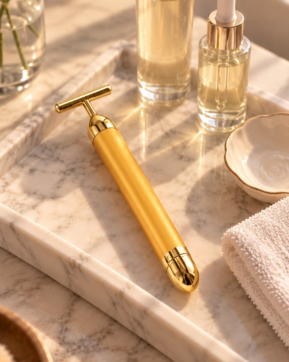 Gold beauty bar on a marble vanity tray beside glass skincare bottles and a folded face cloth